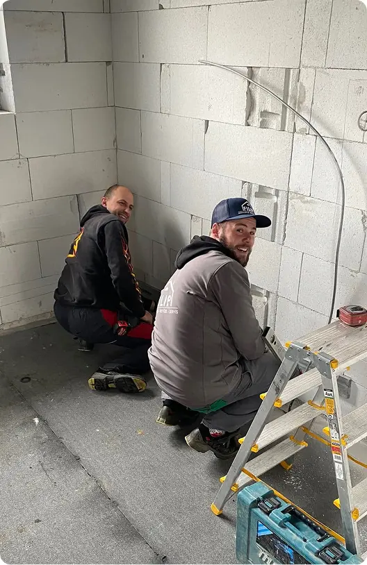 Dvaia usmievaví elektrikári pri inštalácii káblov do steny na stavbe